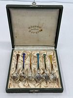 Open case showing six sterling silver demitasse spoons with coloured enamel handles