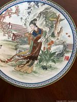 Top-down view of the porcelain plate showing the full painted design of the woman in traditional clothing with the natural background and decorative border.