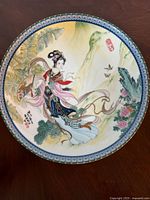Top side of the porcelain plate showing intricate traditional Chinese artwork of a woman with nature elements, bordered with gold trim.