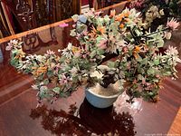 Full side view of the artificial flower arrangement showing pink, orange and green foliage in ceramic pot on wooden table.