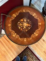 Top view of round wooden table top showing central floral inlay and decorative border with metal edging