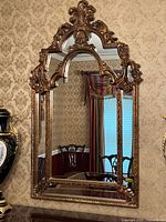 Full front view of the large Baroque gold wall mirror showing the entire framed mirror against a patterned wallpaper background.