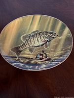 Front view of the porcelain plate showing a detailed artwork of a Smallmouth Bass fish underwater with a fishing reel and rod beneath it.