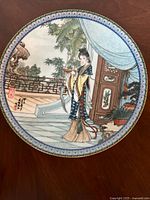 Top view showing the porcelain plate's front with detailed oriental woman holding a tray in a garden setting, surrounded by a blue patterned edge.