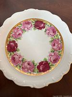 Top view of the decorative plate showing the floral rose pattern with pink and red roses on a white background and scalloped edges.