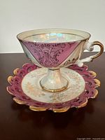 Side view of ornate vintage porcelain teacup on pedestal base with maroon panels and gold detailing