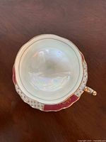 Top view of the teacup showing iridescent white interior, gold trim around rim and red gold-accented handle