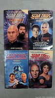 Four Star Trek The Next Generation paperback novels arranged in two rows. Visible titles are Into the Nebula, The Descent, Masks, and Guises of the Mind.
