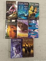 Top front covers of the eight Star Trek: The Next Generation novels arranged on a surface, showing cover artwork featuring characters and starships.