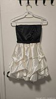 Front view of black bodice and white tiered skirt strapless dress on hanger