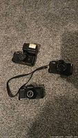 Three Pentax cameras and flash unit laid out on carpet
