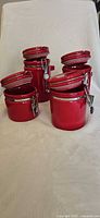 Four red ceramic canisters with lids open, showing sizes