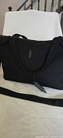 Front of black Thacker weekender bag showing logo leaf zipper pull and handles
