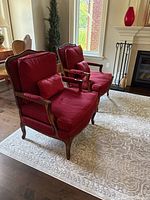 Pair of red upholstered bergère chairs with carved wooden frames on area rug