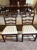 Two wooden dining chairs with ladder backs and upholstered seats placed on a rug in front of a dining table set.