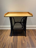 Front view of the antique sewing machine base with pine tray table top, showing the iron base design and pine surface.