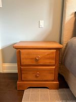 Full front view of the solid wood bedside table showing two drawers with wooden knobs and base.