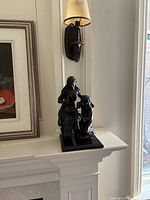 Bronze statue shown on a white mantel near a wall sconce, depicted from a side angle.