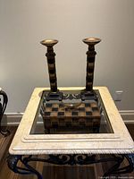 Pair of tall candle sticks and matching decorative box on marble and iron table, showing black and gold checkered pattern