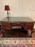 Front view of desk showing burl veneer finish, glass top, brass hardware