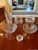 Overall set of clear glassware showing two vases, three bowls, and one candle holder on wooden table.