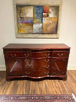 Full front view of antique wooden dining room buffet showing curved shape and drawer/cabinet configuration.