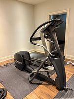 Precor elliptical shown from the side on a black exercise mat, highlighting the frame, pedals, and digital console.