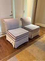 Pair of blue upholstered chairs with brown piping side by side on wooden floor near window.