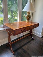 Full view of the wooden desk placed near window with lamp on top.
