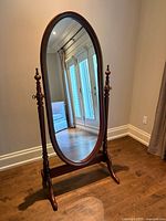 Front view of full-length wooden oval stand-up mirror with turned posts and curved base.