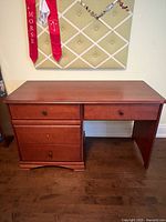 Front view of solid wood desk showing four drawers; one knob missing on one drawer.