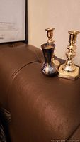 Two brass candlesticks and silver bud vase grouped on leather surface