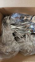 Box containing bagged stainless flatware showing variety of utensils