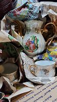 Teapot and partially visible teacup in packing, showing gold handles and courting scene