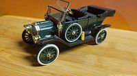 Front three-quarter view of green and gold early 1900s touring car model showing grille, lamps, and wheels