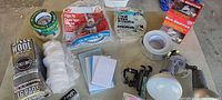 Packaged tapes, steel wool, foam tape, weatherseal, rug grippers, duct tape, clamps and puck lights on table