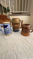 Three ceramic steins: blue-white German, Viking head, brown relief