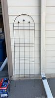Black metal arched trellis leaning against siding