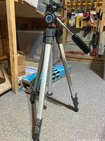 Tripod standing on floor, legs extended, pan-tilt head and handle visible