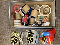Top view of open box showing assorted tape rolls, dispensers, Alien Tape packs and Scotch pack