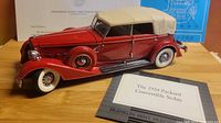 Left front view of red 1934 Packard model with beige soft top, certificate in background