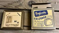 Front view of metal calendar coin bank beside original Safecoin box