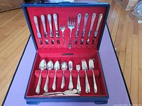Full open wooden box displaying the 66-piece set of 1847 Rogers Bros silverplate flatware in the Adoration pattern with red velvet lining.