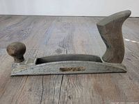 Side view showing the full length of the Stanley Surform rasp with wooden front knob and rear grip handle, placed on a wooden floor.