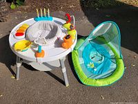 Photo of baby activity centre and SwimWays baby pool floaty placed outdoors on asphalt surface.
