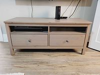 Full frontal view of Ikea TV bench showing two drawers with round knobs and two open shelves above, placed on wooden floor.