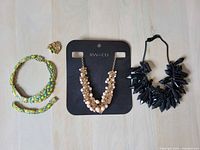 Braided turquoise and yellow beaded necklaces, pearl cluster earrings on RW&CO card, and black spike necklace arranged on flat surface.