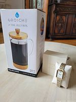 Photo of the boxed Grosche Melbourne coffee and tea press along with the Larrson & Jennings watch on a cushion and its box nearby