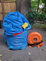 Deflated inflatable and accessories inside blue carrying bag next to orange blower fan