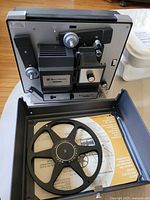 Bell & Howell Super 8 projector front and side view with film reel, showing controls and mechanical parts